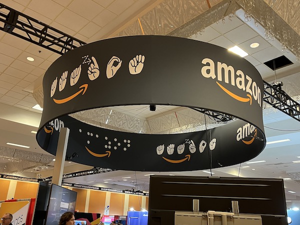 An Amazon sign hanging over their exhibit at the CSUN conference. The sign has Amazon spelled in standard letters, as well as braille and American Sign Language.